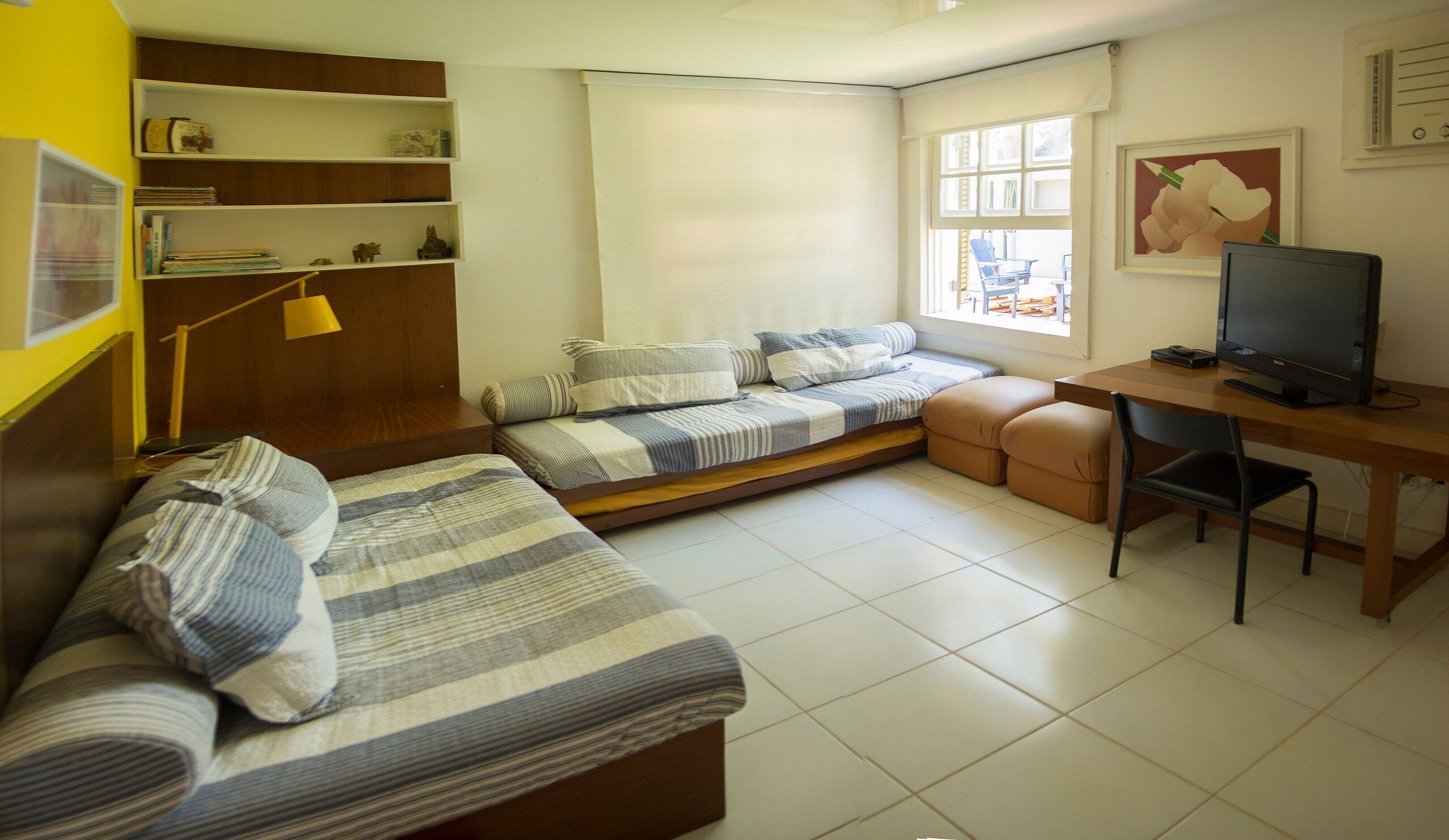A compact living space with a sofa bed, a desk with a computer, and a window with a view of the outdoors.