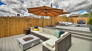 Eine Terrasse im Freien mit Holzdeck, einem weißen Sofa, einer Feuerstelle und einem großen Sonnenschirm.