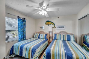 Une chambre avec deux lits, un ventilateur de plafond et un motif décoratif représentant des poissons sur le mur.