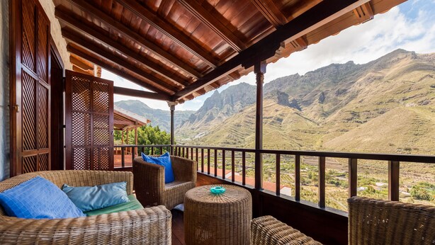 Un balcón con muebles de mimbre, un otoman redondo y vistas a las montañas.
