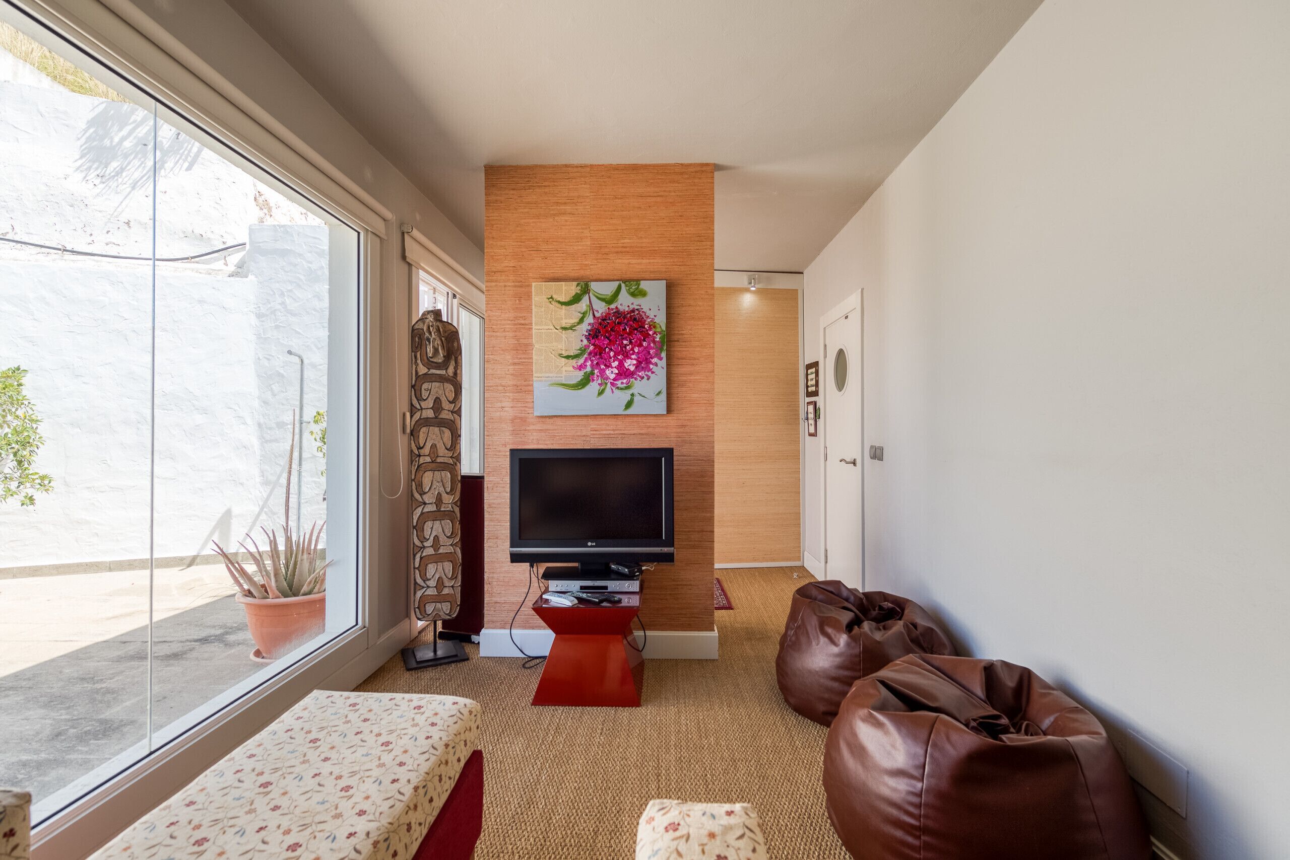 Ein modernes Wohnzimmer mit Flachbildfernseher, einer Holzwand, einem großen Fenster und einem Blumentopf.