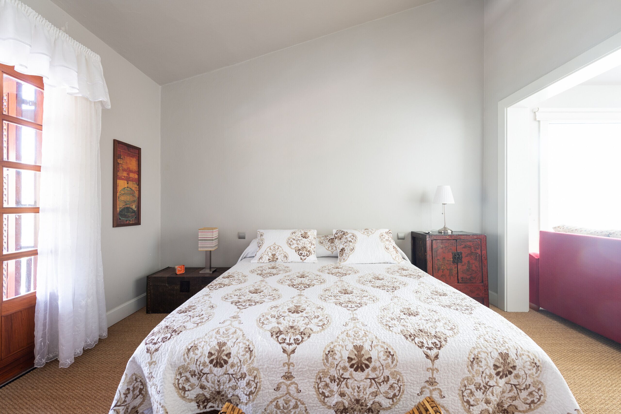 Ein Schlafzimmer mit einem großen Bett, einem Nachttisch, einer Kommode und einem Fenster mit Vorhängen.