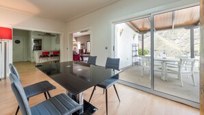 Un comedor amplio con una mesa grande y sillas, una cocina al fondo y vistas a un patio con mobiliario exterior.