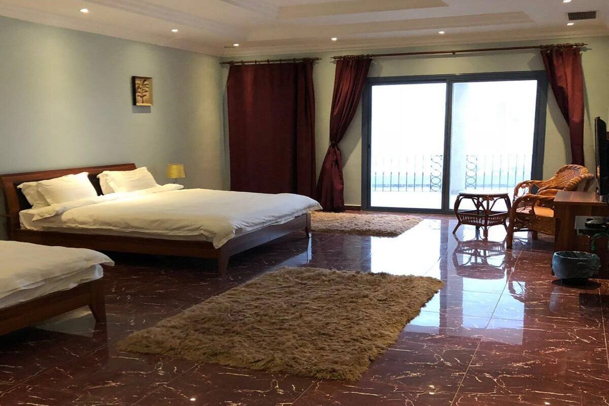 A hotel room with a large bed, a smaller bed, a sofa, a chair, a TV, and a balcony with a railing.
