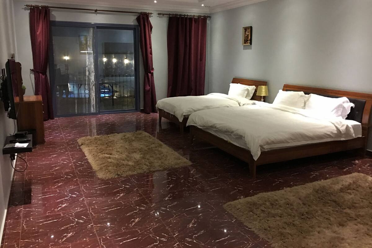 A hotel room with a large bed, a small bedside table, a lamp, and a view through a glass door.