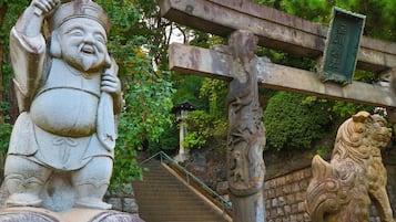 Una estatua de piedra de una figura sosteniendo una taza, una estatua de león y una escalera que conduce a una estructura verde.