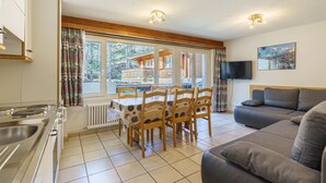 A kitchen with a stove, a dining table with chairs, a sofa, and a TV on the wall. - Haus-Alfa (Saas-Fee)