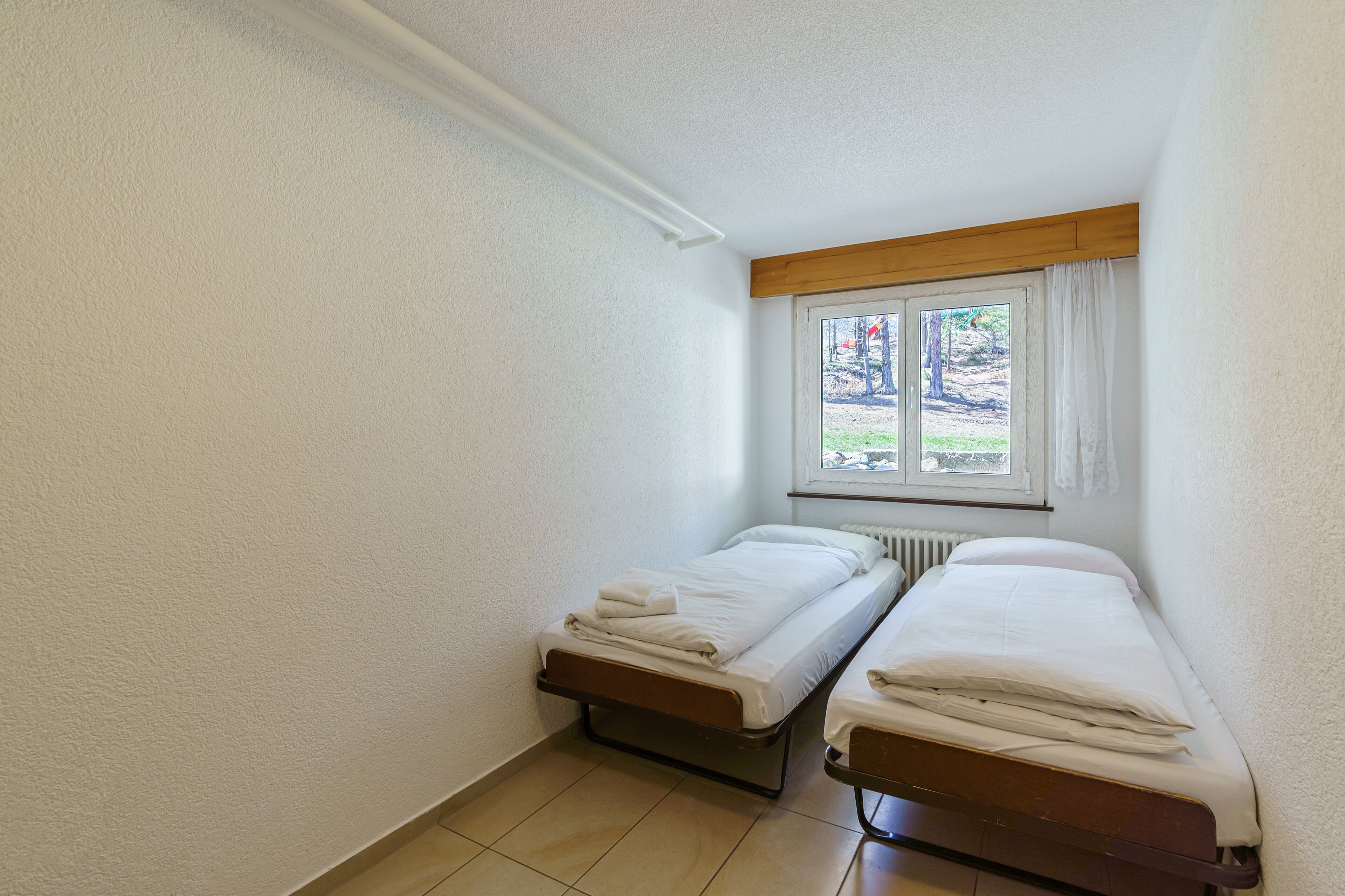 A small, clean room with two single beds, a window with curtains, and a radiator.