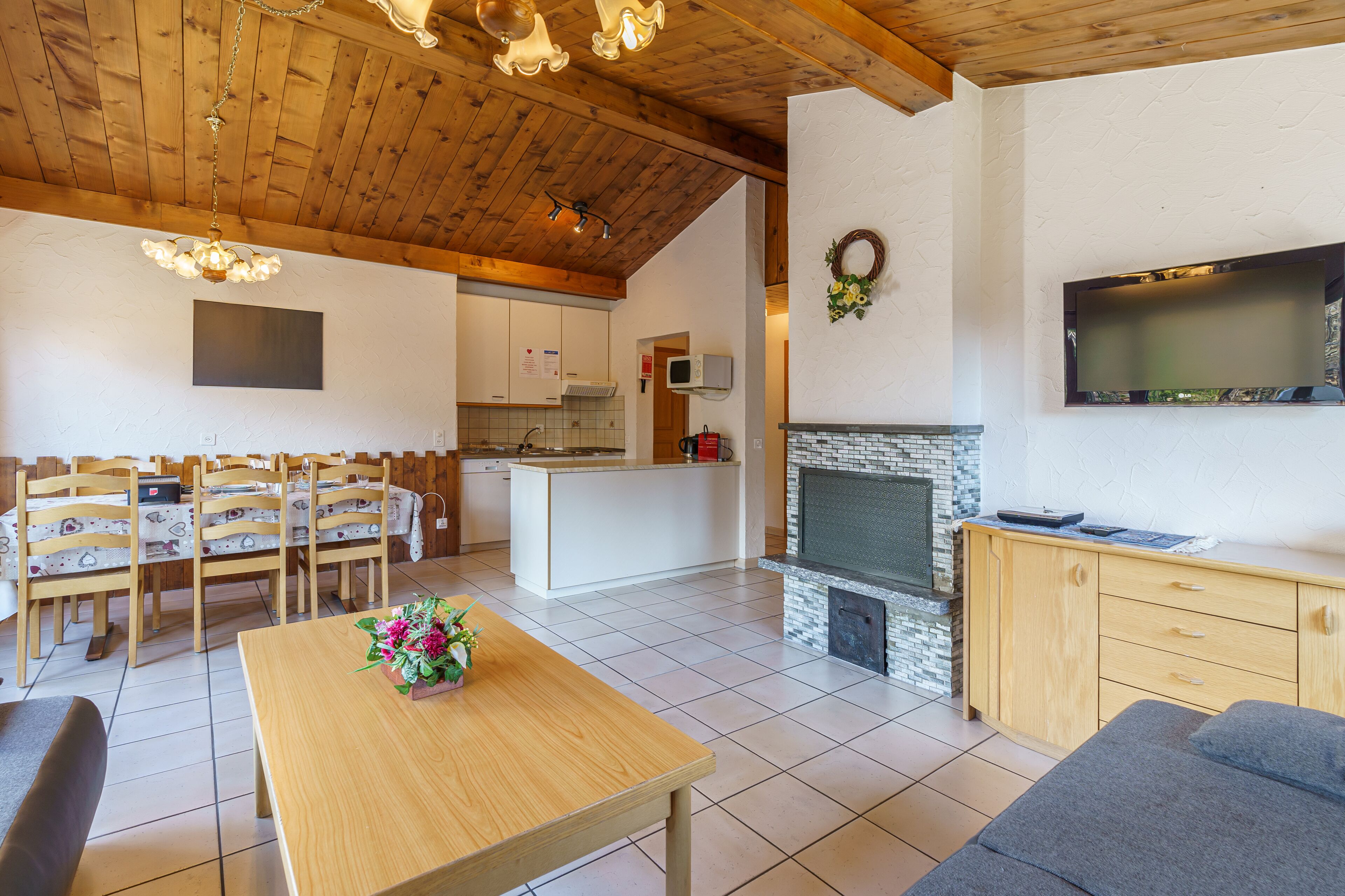 Un espacio habitable amplio con techo de madera, chimenea, mesa de comedor con sillas y televisor montado en la pared.