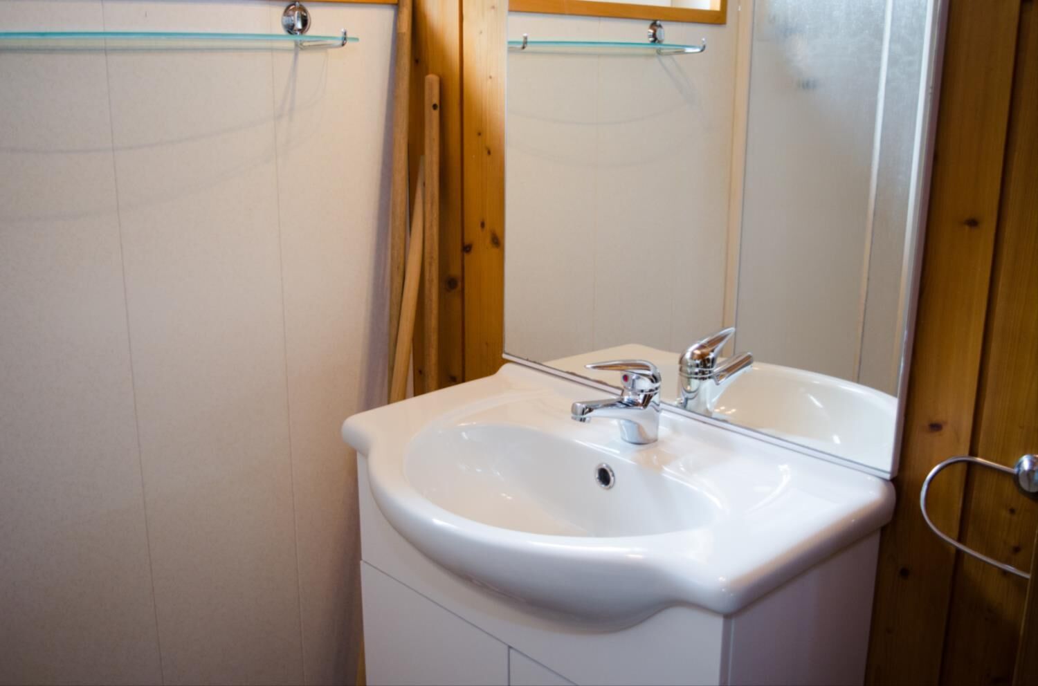 Een badkamer met een witte wastafel, een chromen kraan en een glazen plank boven de spiegel.