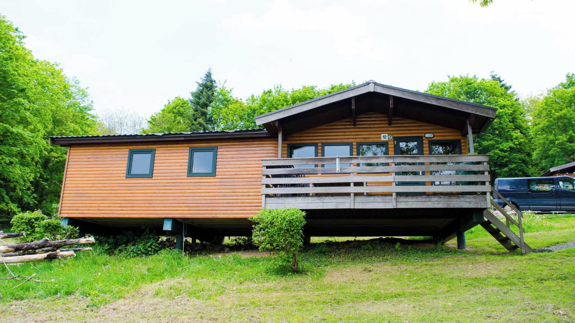 A wooden cabin with a balcony, surrounded by greenery.