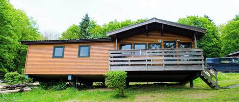A wooden cabin with a balcony, surrounded by greenery.