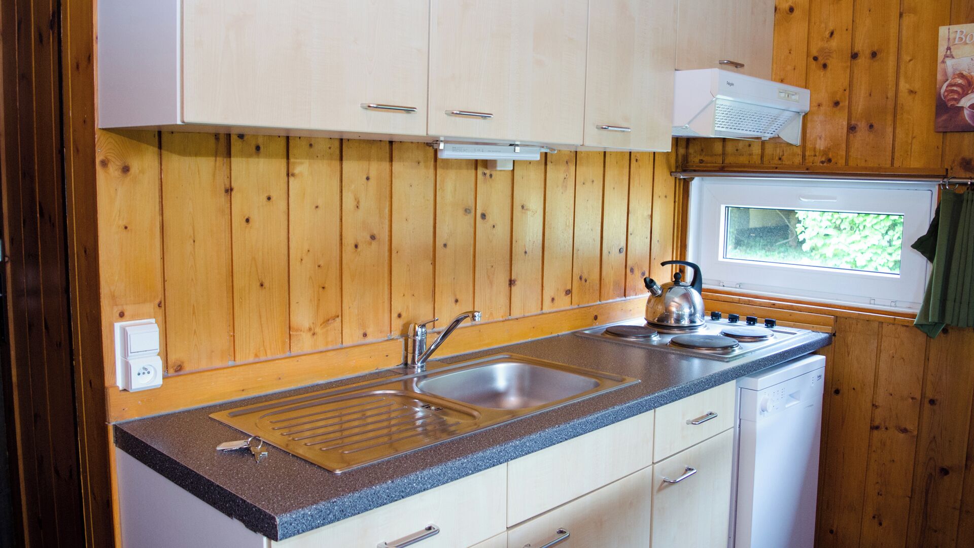 A compact kitchen with wooden panel walls, a sink, stove, and a window providing natural light.