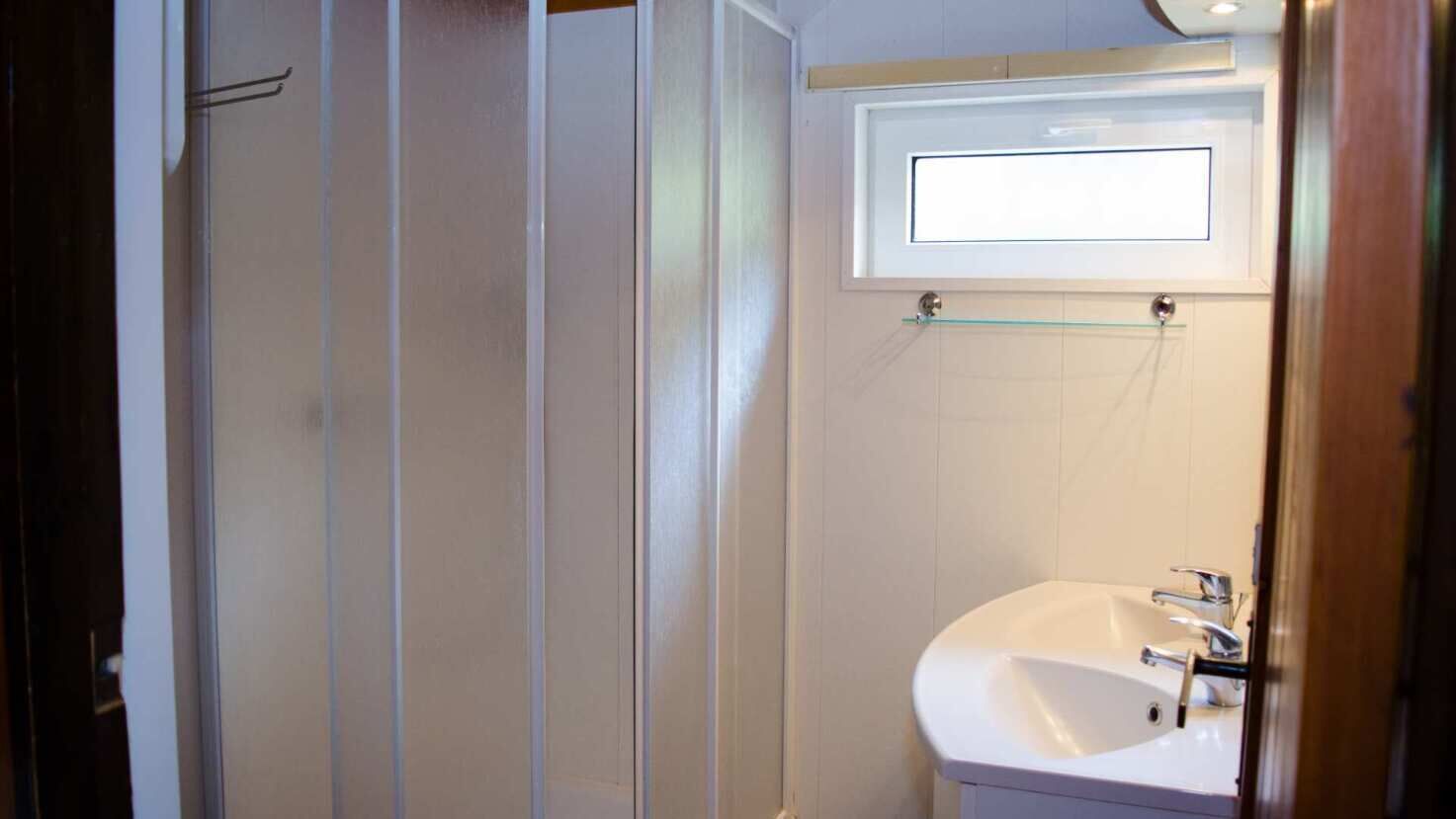 A bathroom with a white sink, a mirror, and a glass shelf above the sink.