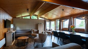 Una habitación acogedora con techo de madera, un sofá, sillas, una mesa de comedor y un televisor fijado en la pared.