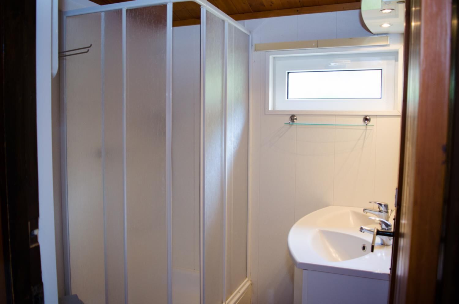 A bathroom with a shower enclosure, a sink, and a small window above the mirror.