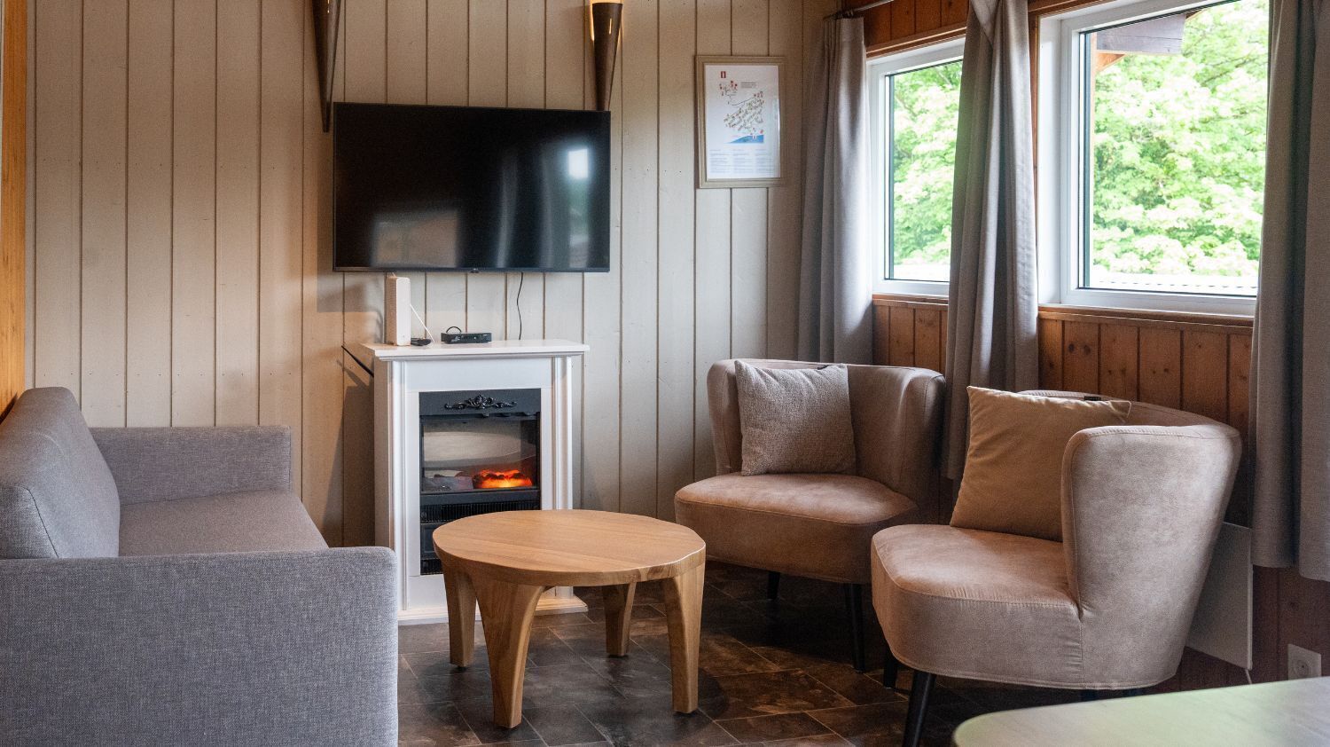 Une pièce confortable avec un téléviseur à écran plat fixé au mur, une cheminée et deux fauteuils rembourrés.