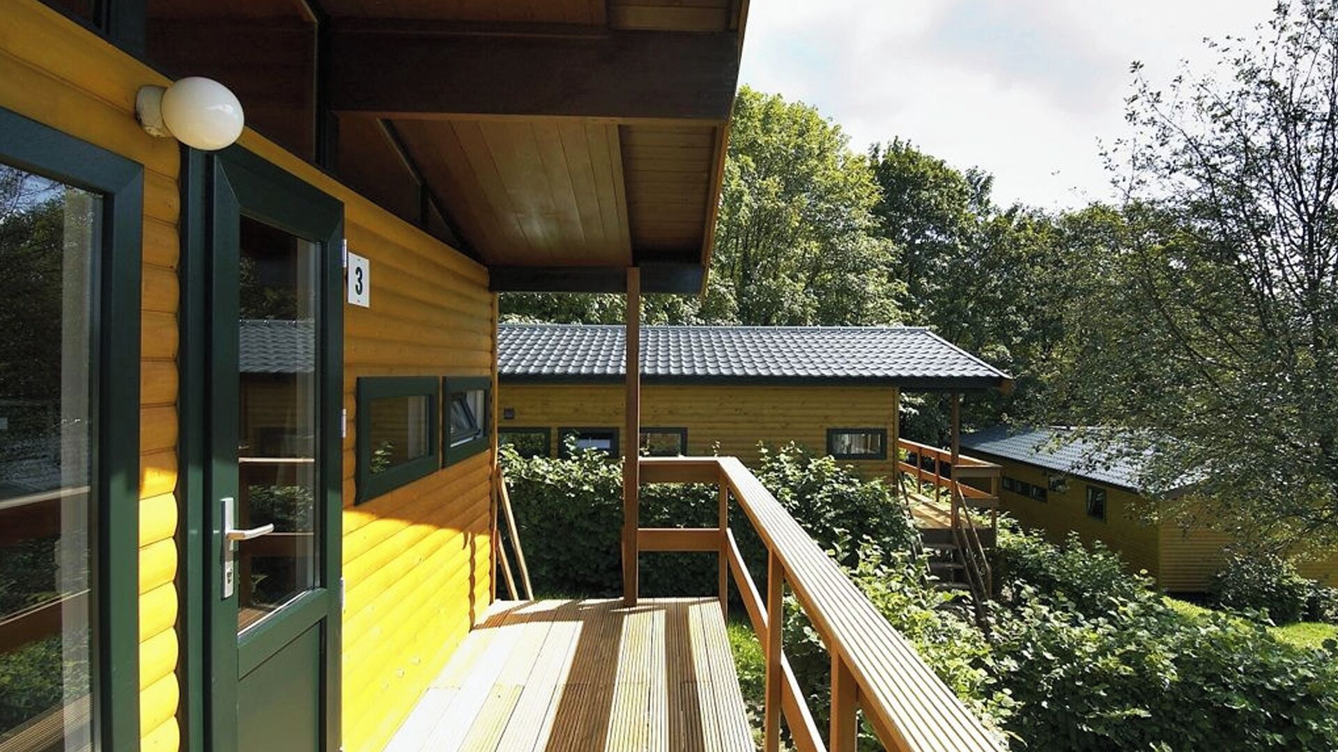 Una cabaña de madera con balcón, terraza cubierta y vista a árboles circundantes.