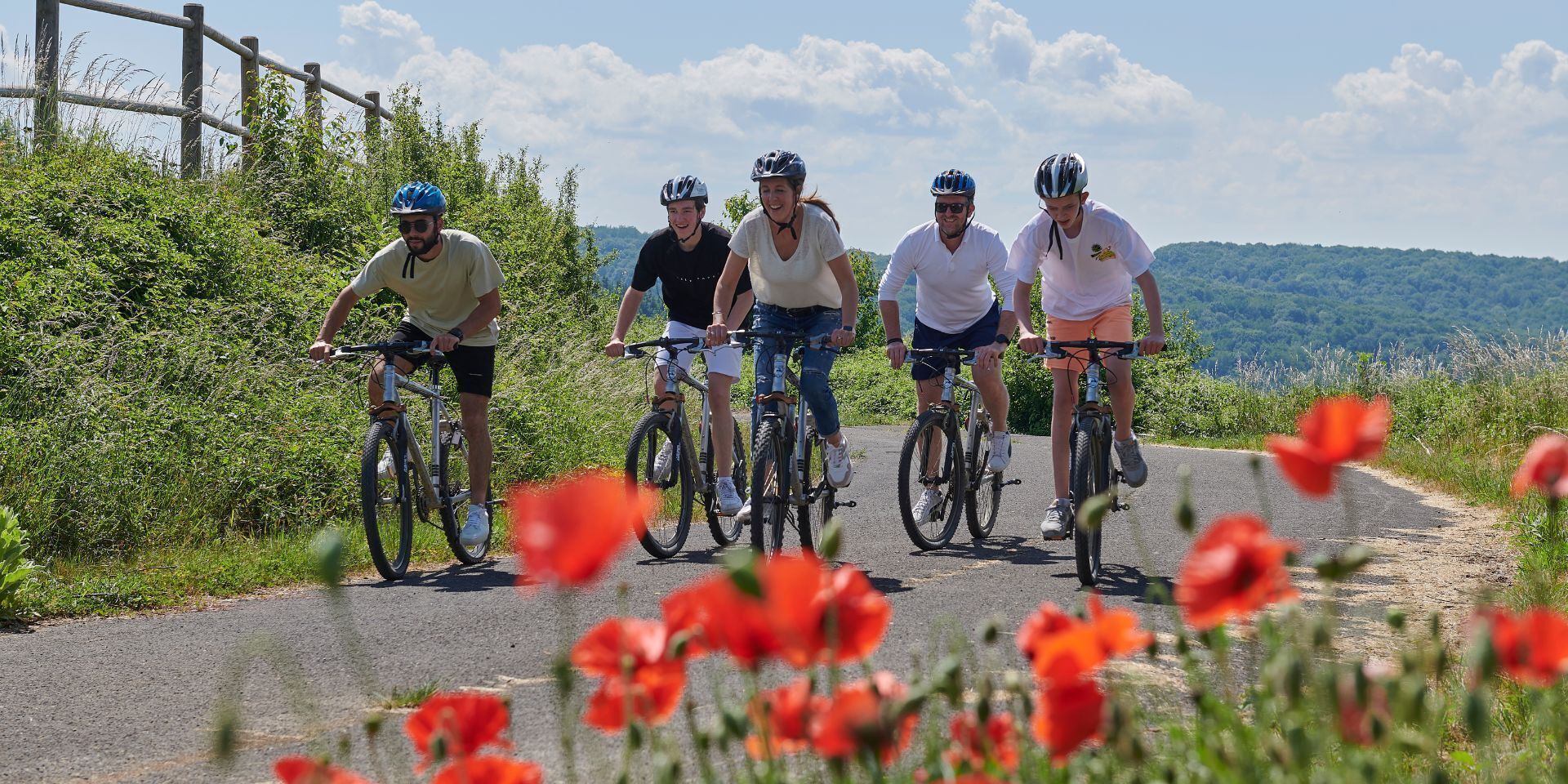 Een groep fietsers op een verharde weg met een landelijk landschap en rode bloemen op de voorgrond.