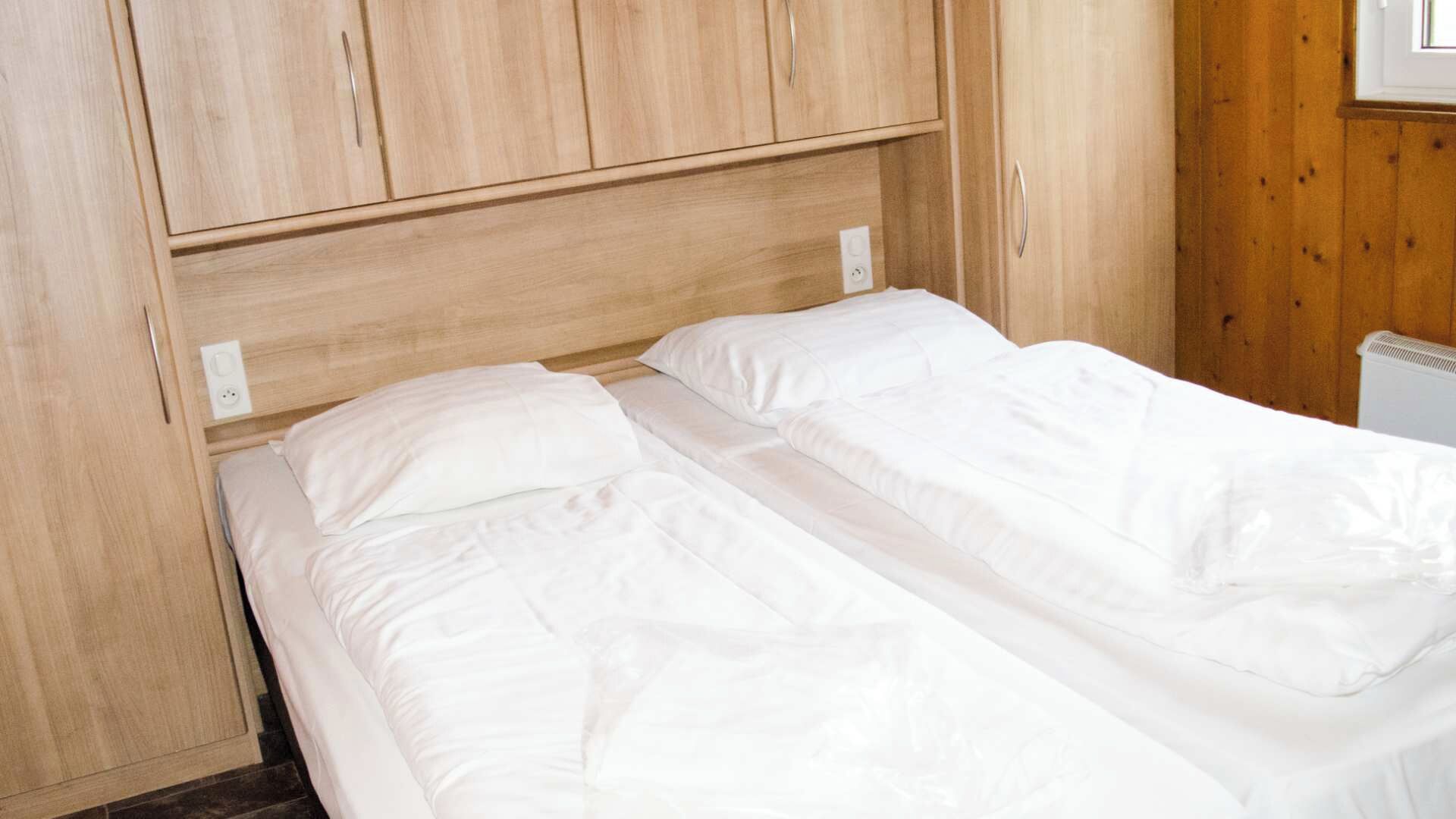 A single bed with white bedding in a room with wooden walls and a simple headboard.