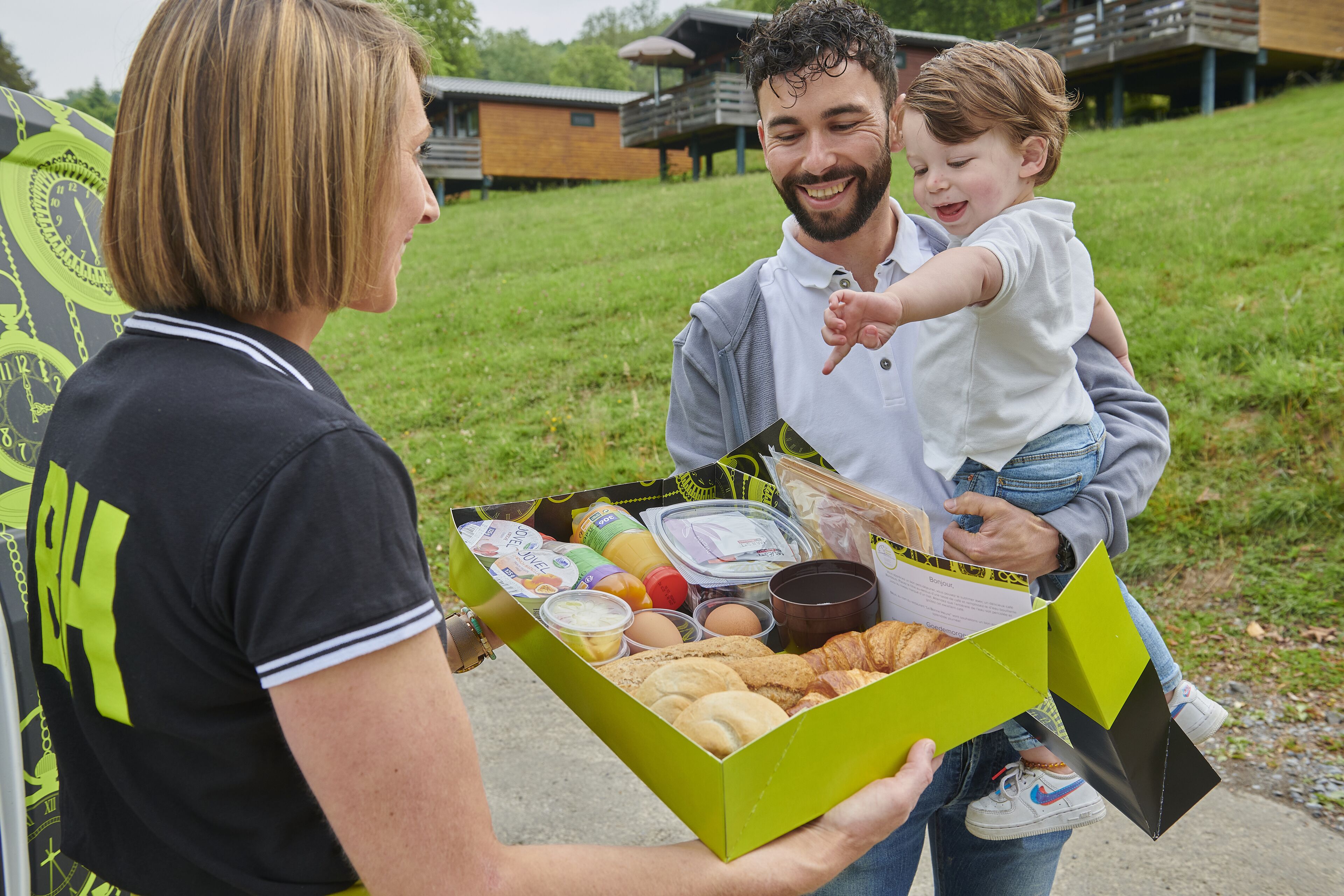 A person holding a box with food items and a child on their back.