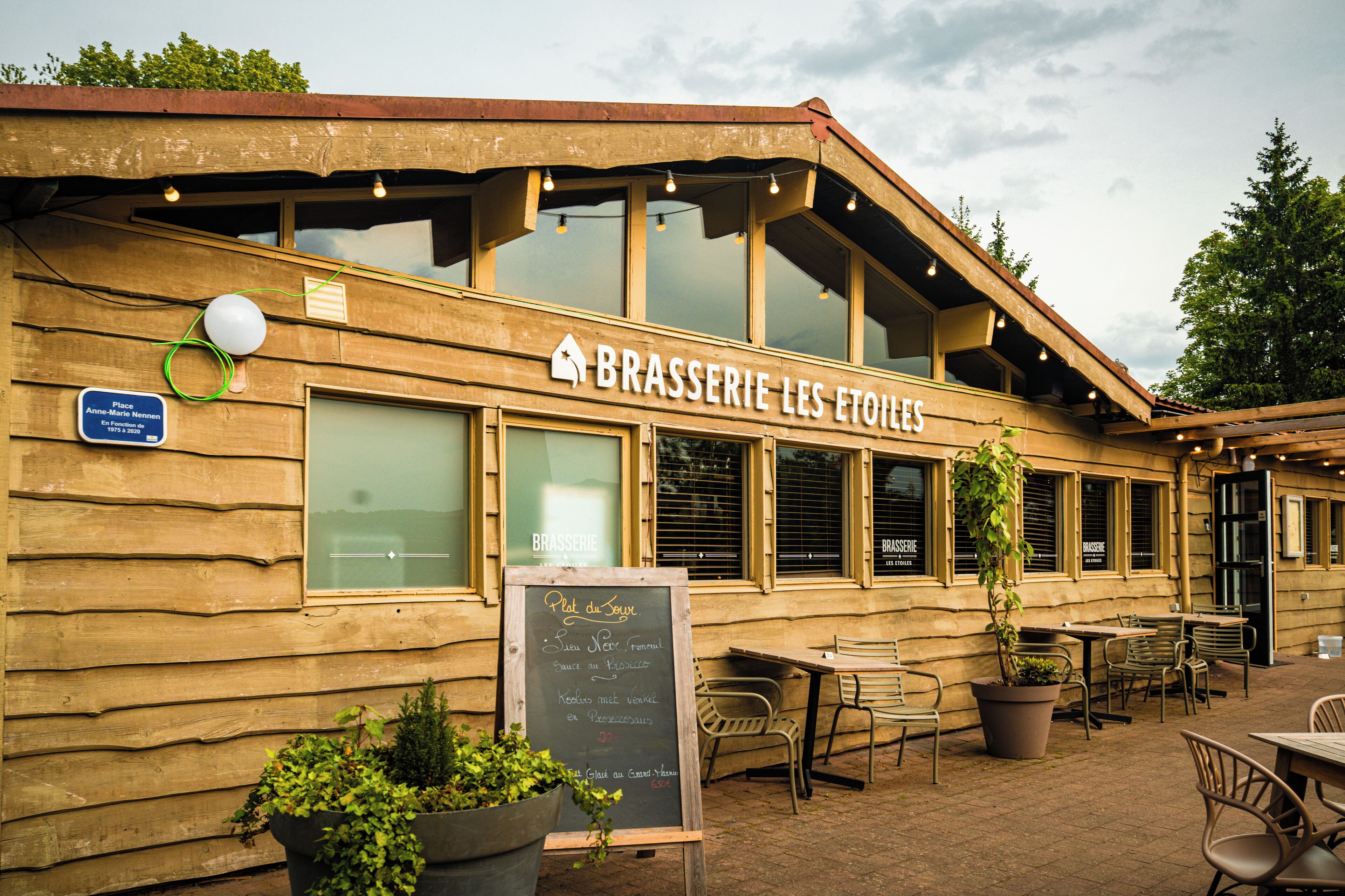 A wooden exterior of a restaurant named 'BRASSERIE LES ETOILES' with outdoor seating and a chalkboard menu.