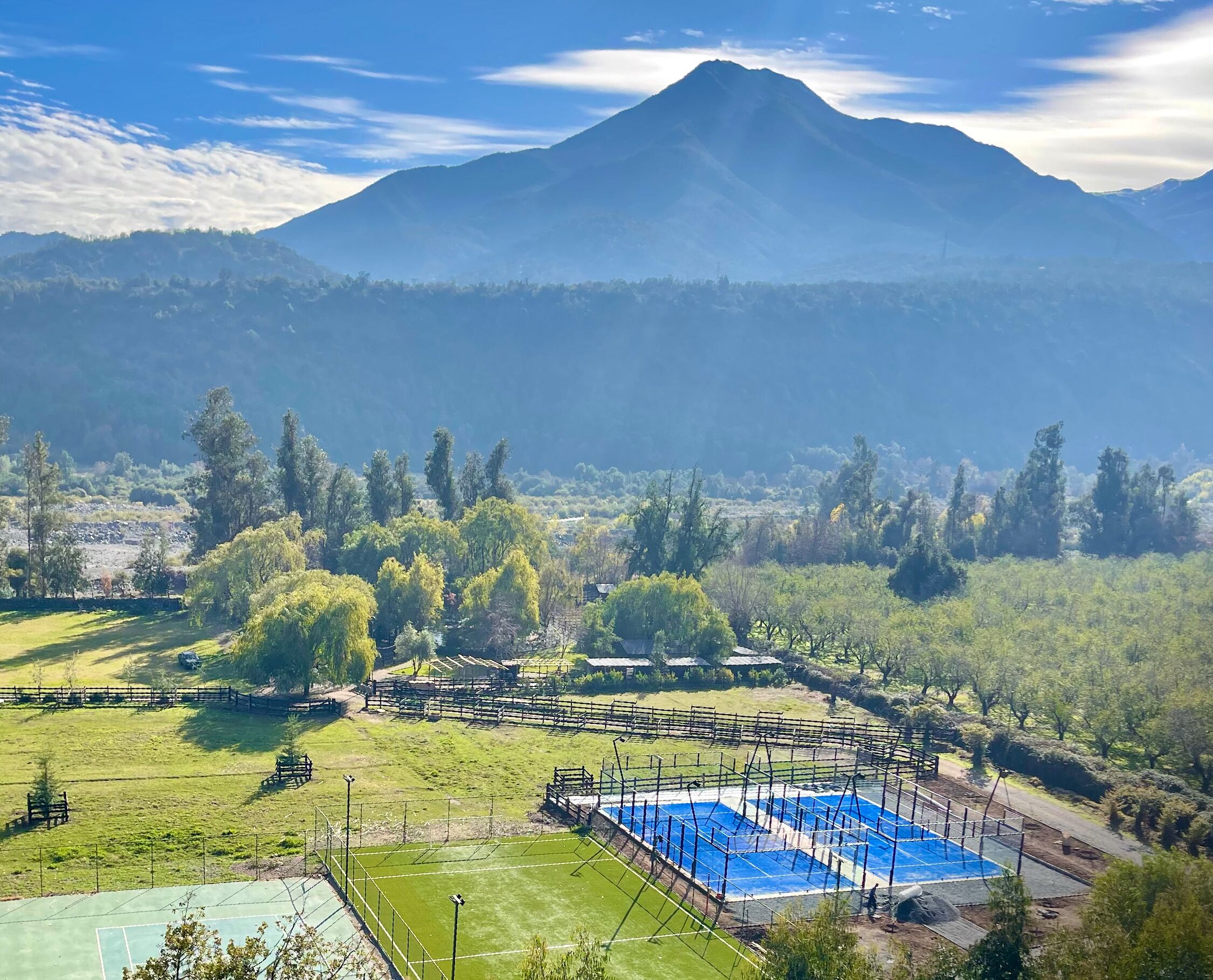A tennis court with a net, surrounded by a fence, and a mountain in the background.