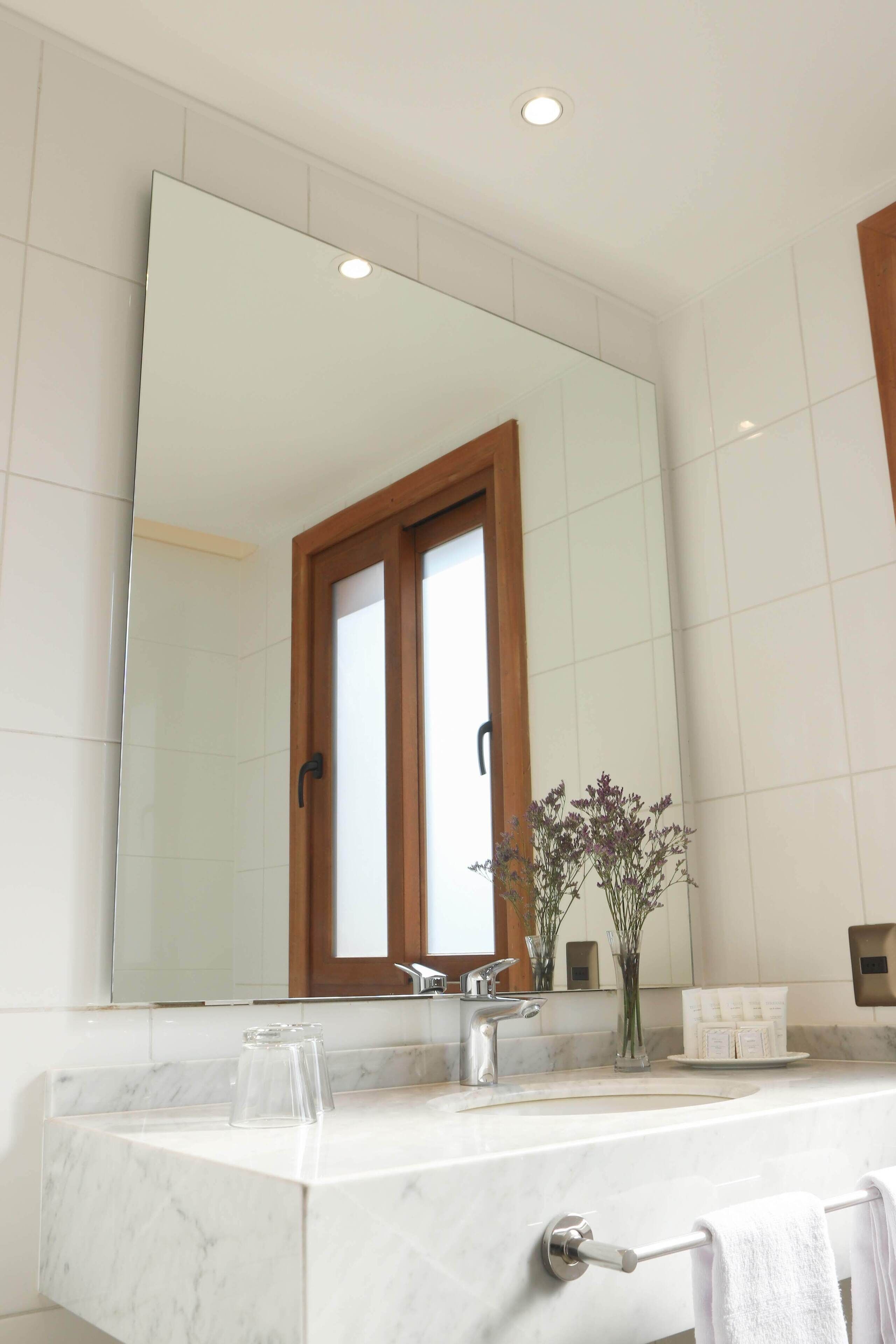 A bathroom with a large mirror, a marble countertop, a towel rack, and a small vase with flowers.