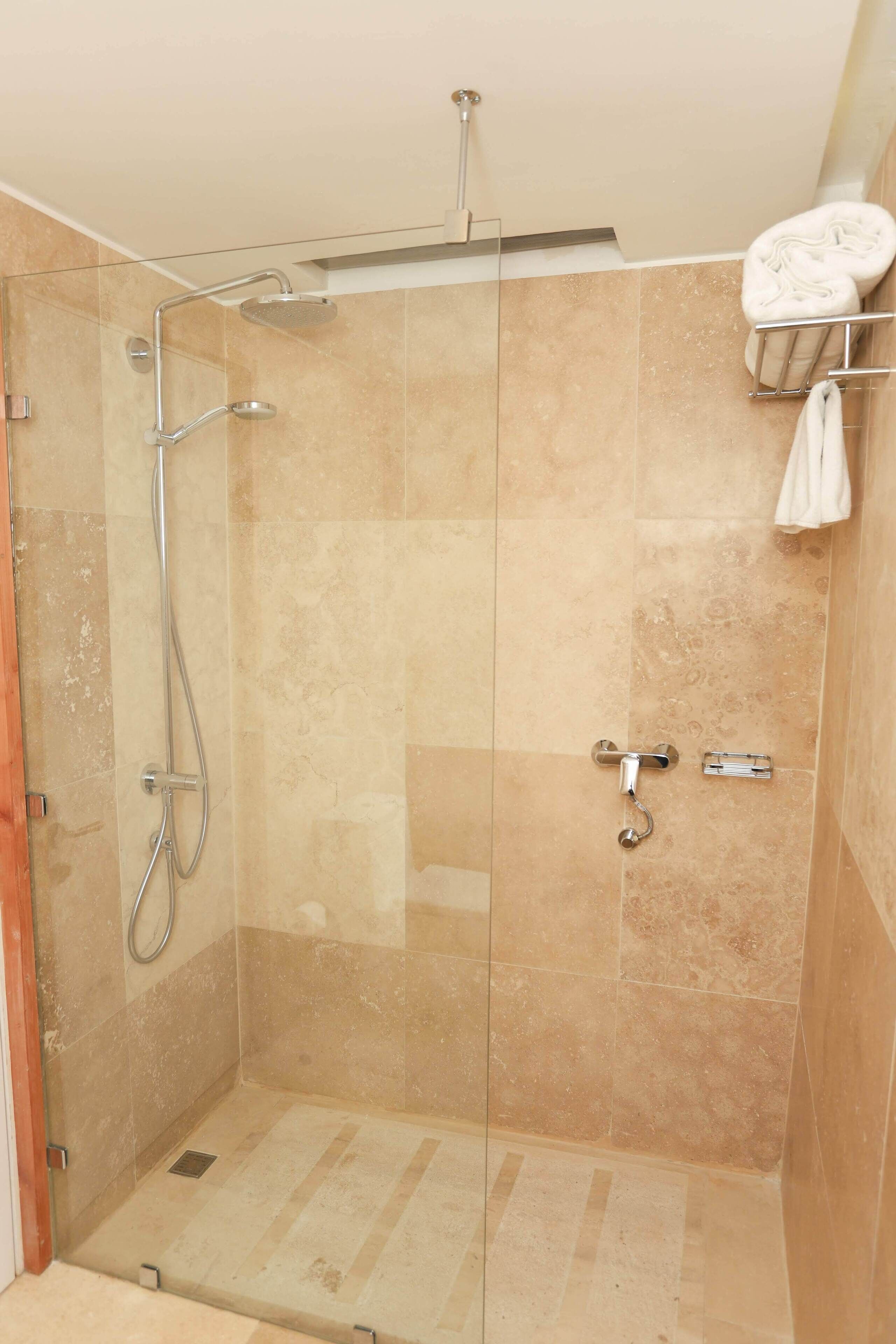 A glass-enclosed shower with a handheld showerhead and a wall-mounted faucet.