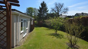 A residential property with a well-maintained lawn, a wooden pergola, and a variety of trees and shrubs.