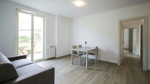 A modern living room with a sofa, a dining table with chairs, and a large sliding glass door leading to an outdoor area. - Apartment "E" Balcony - Levanto Cinque Terre (Levanto)
