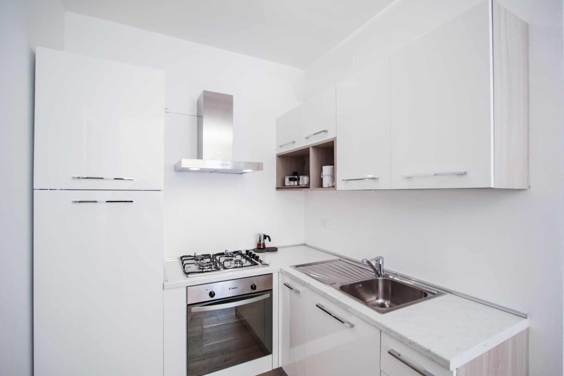 Una cucina moderna con mobili bianchi, piano cottura a gas, forno e lavello in acciaio inossidabile.