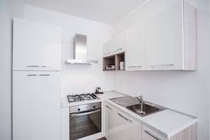 Una cocina moderna con muebles blancos, estufa a gas, horno y pileta de acero inoxidable.