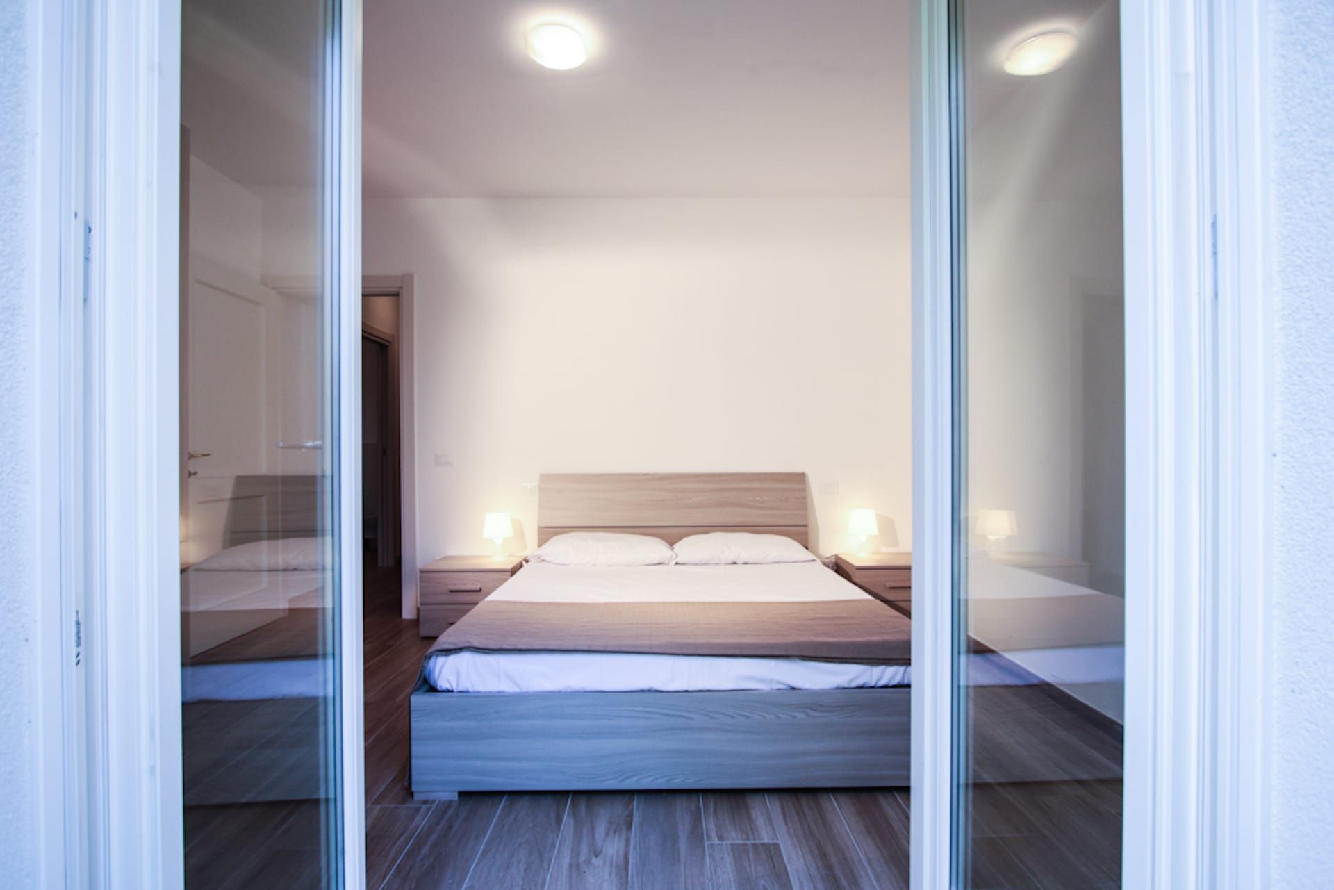 Una camera da letto con un letto, lampade ai comodini e una porta che dà su un'altra stanza.