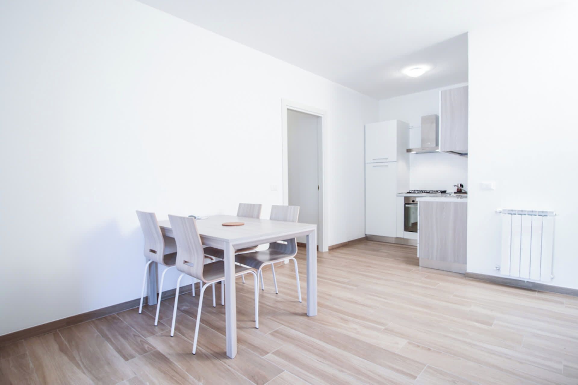 Un appartement moderne et minimaliste comprenant un coin repas, une cuisine et une porte donnant sur une autre pièce.