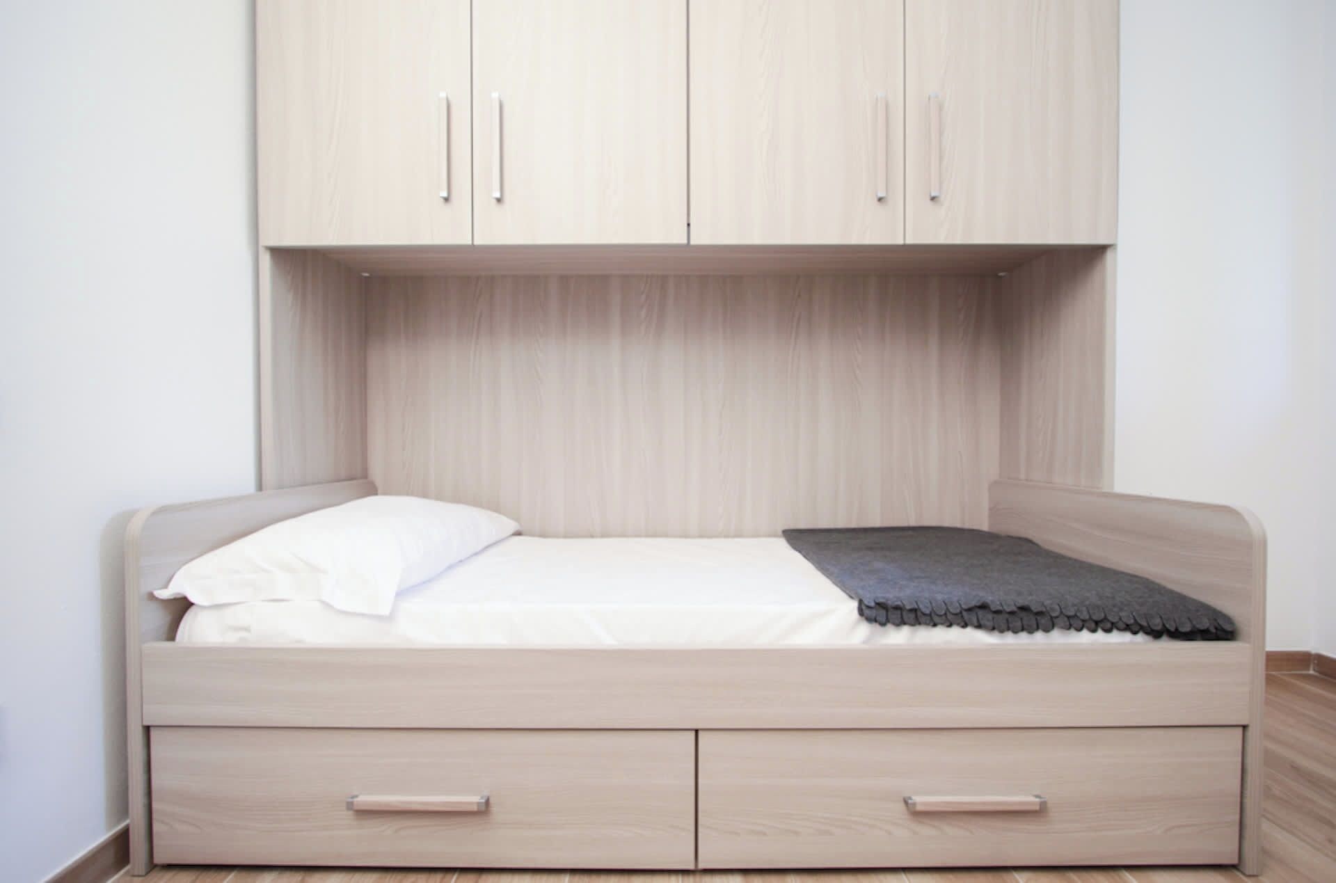 Un lit simple avec une tête de lit, deux tiroirs et un placard au-dessus.