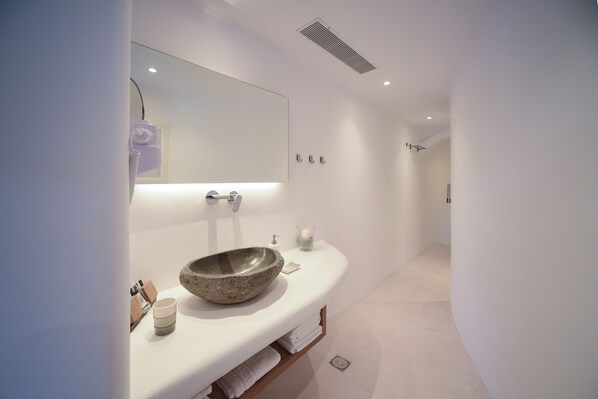 A modern bathroom with a large mirror, a stone basin, and a white countertop.