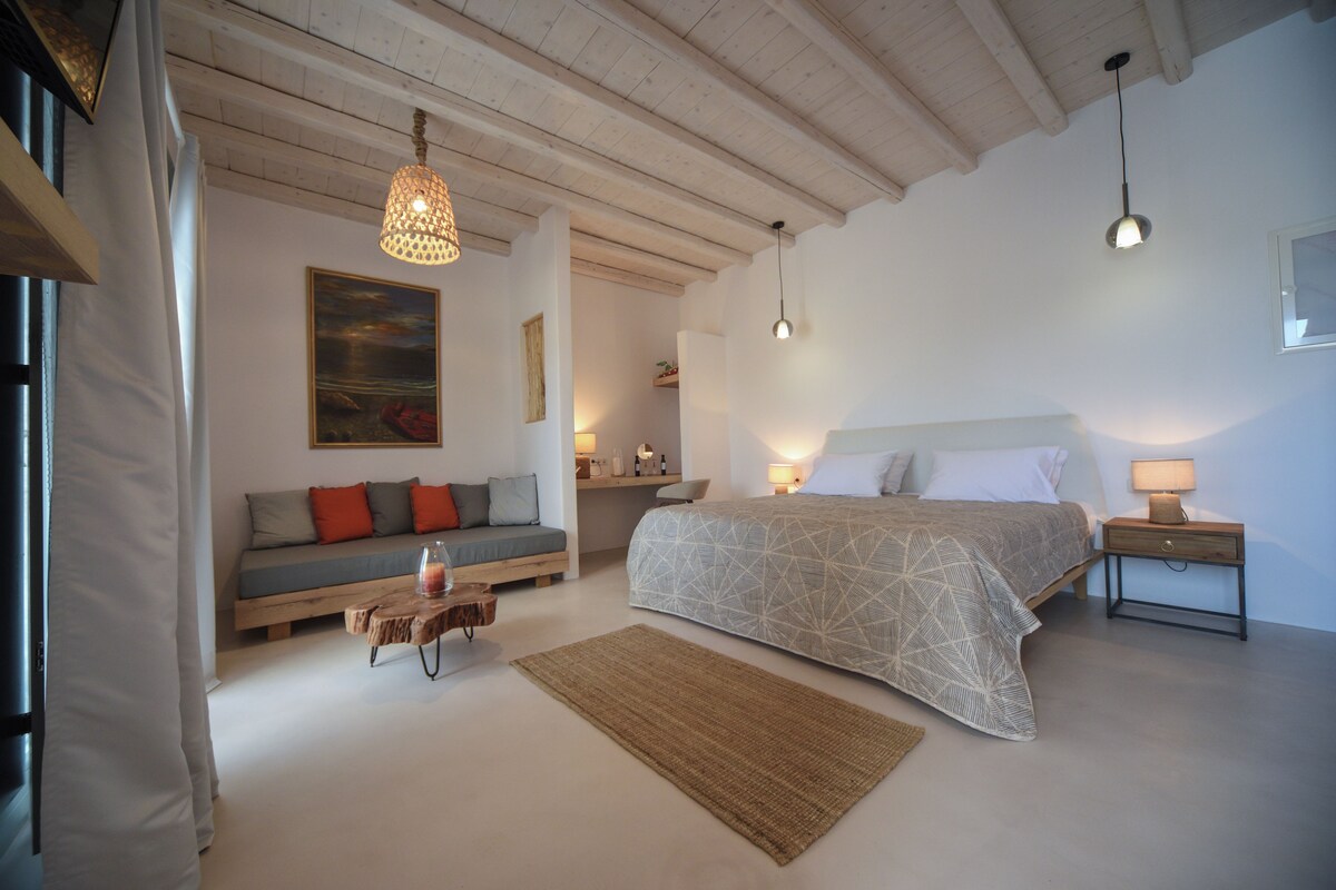 A bedroom with a bed, bedside tables, a sofa, a wooden coffee table, and a painting on the wall.