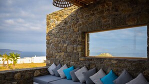 A stone wall with a window overlooking a coastal view. - Myconian Crown Suites by Mr and Mrs White (Mykonos)