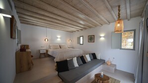 A bedroom with a bed, bedside tables, a bench, and a hanging light fixture. - Myconian Crown Suites by Mr and Mrs White (Mykonos)