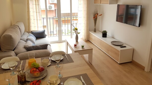 Ein modernes Wohnzimmer mit einer Couch, einem Esstisch für zwei Personen und einem an der Wand befestigten Fernseher.