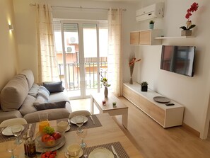 A modern living room with a sofa, dining table set for two, and a TV mounted on the wall.