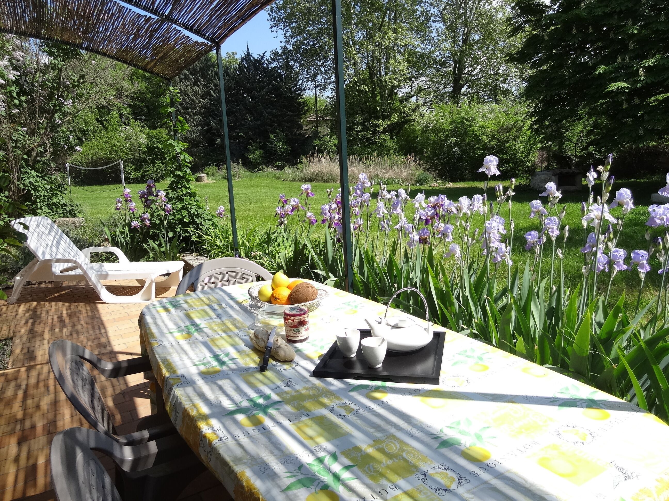Un área de comedor al aire libre con una mesa dispuesta para dos personas, rodeada de exuberante follaje y flores en flor.
