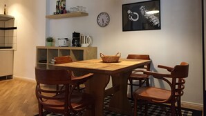 A dining area with a wooden table, four chairs, a hanging light, a clock, and a shelf with kitchen items. - Loft 1. 3 in the heart of Berlin (Bezirk Friedrichshain-Kreuzberg)
