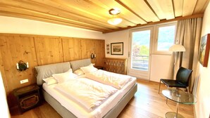 Et soveværelse med træloft, en seng med hvide sengetøj, et glastilbord og en stol.