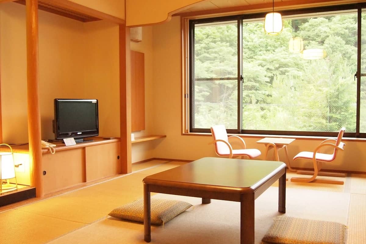 A traditional Japanese room with tatami flooring, a television, a table, and chairs.