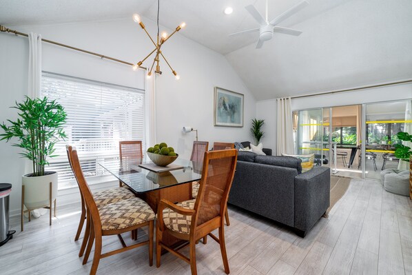 A modern living room with a glass dining table, wooden chairs, a grey sofa, and a ceiling fan. - Charming 2BR/2BA Villa With Golf Course View! NO pets (Johns Island)