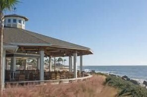A coastal building with a circular tower, a covered patio with seating, and a view of the ocean. - Charming 2BR/2BA Villa With Golf Course View! NO pets (Johns Island)
