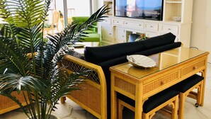 A living room with a television on a white stand, a sofa, a coffee table, and a large potted plant. - SHELLebrations: Gulf-Front Penthouse Paradise on Fort Myers Beach, Florida (Fort Myers Beach)