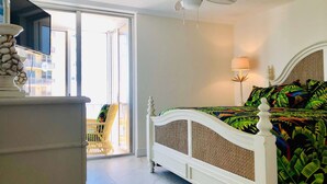 A bedroom with a white bed, a ceiling fan, a window, and a view of the outside balcony. - SHELLebrations: Gulf-Front Penthouse Paradise on Fort Myers Beach, Florida (Fort Myers Beach)